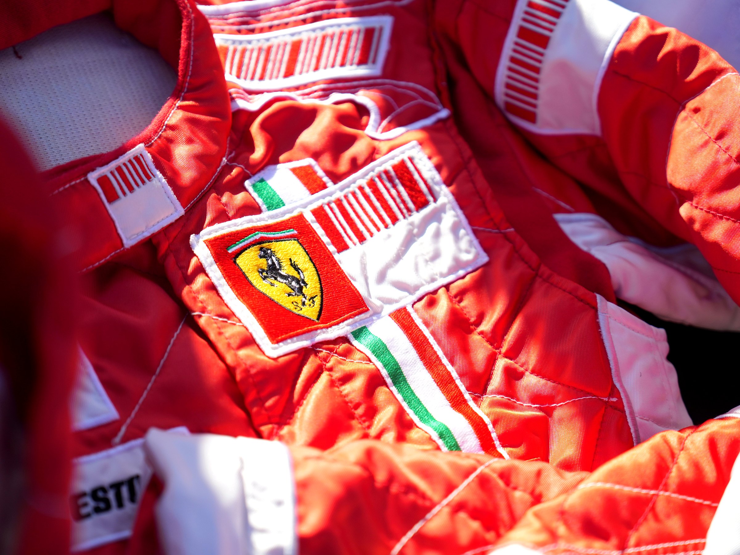 Close-up of a red Ferrari racing suit with team badges, displayed as collectible memorabilia